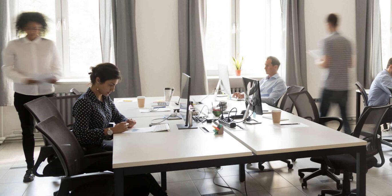 Mehrere Personen arbeiten konzentriert an modernen Schreibtischen mit Monitoren in einem hellen Büro.