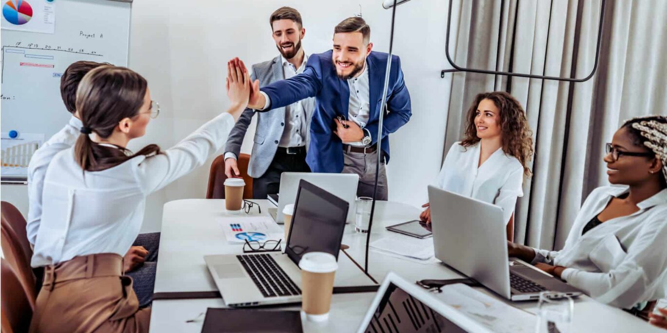 Teammitglieder im modernen Büro geben sich ein High-Five während einer Besprechung, was den positiven Einfluss moderner Büroumgebungen auf HR-Prozesse verdeutlicht.