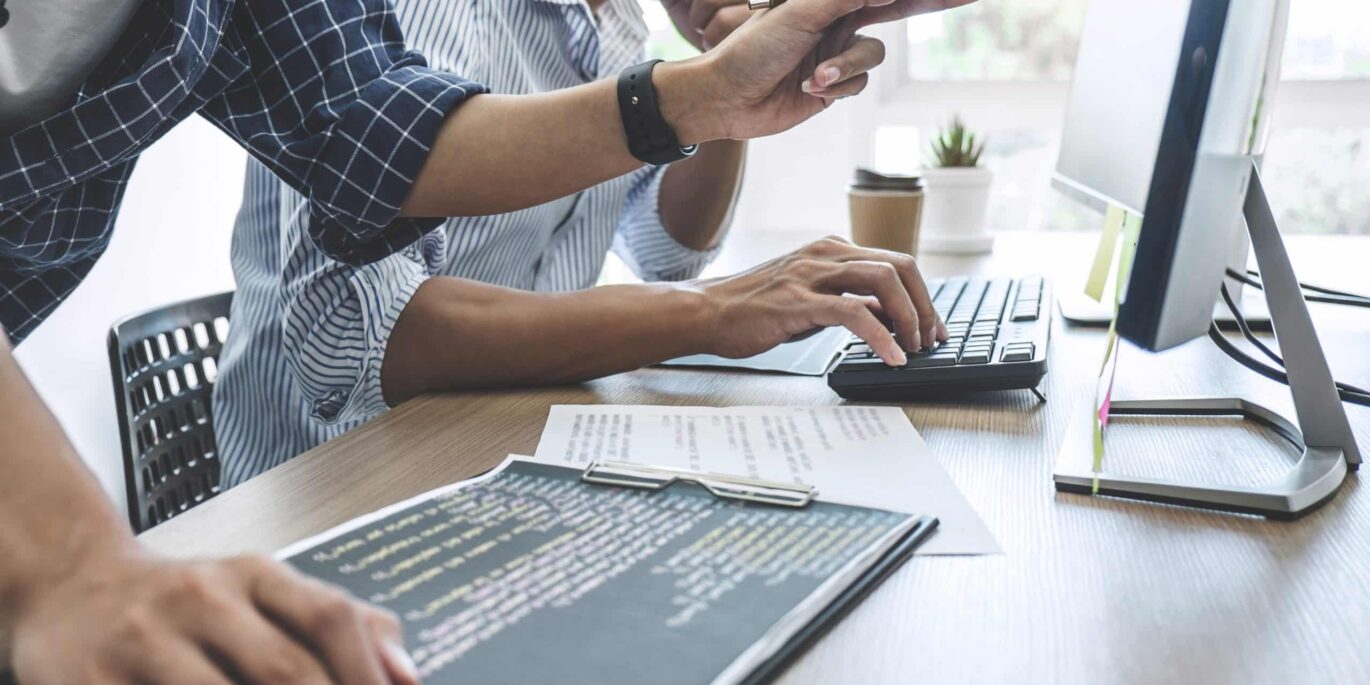 Zwei Personen arbeiten zusammen am Computer, eine zeigt auf den Bildschirm, während die andere tippt – Symbolbild für Zeitfresser im Büro