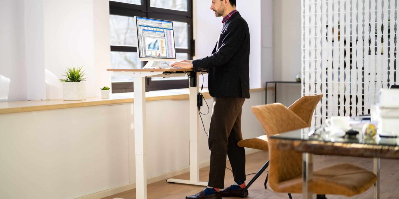 Mann arbeitet konzentriert an einem höhenverstellbaren Schreibtisch im Stehen – Beispiel für ergonomische Büroeinrichtung.