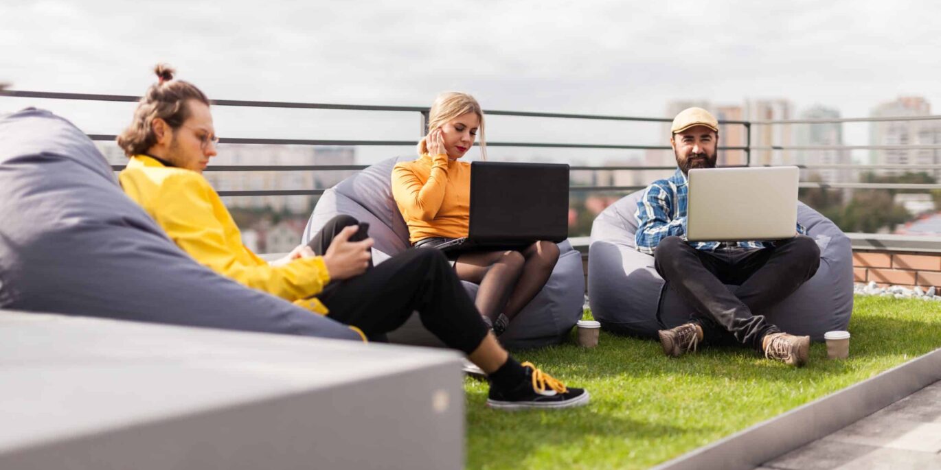 Drei Personen arbeiten mit Laptops entspannt im Außenbereich auf Sitzsäcken auf einer Dachterrasse.