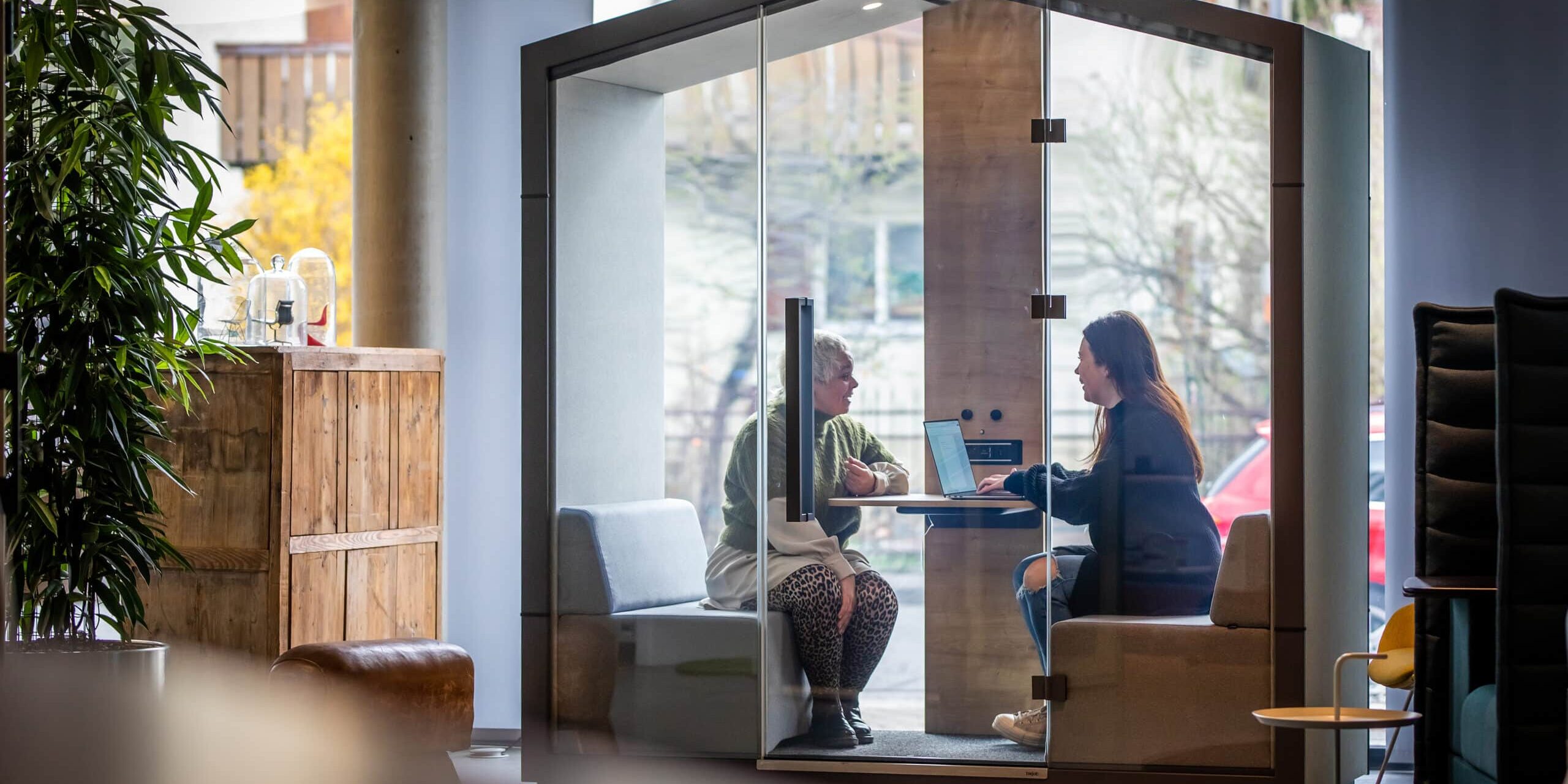 Zwei Frauen arbeiten in einer akustisch abgeschirmten Meetingbox mit Laptop in einem modernen Büro – typische Szene im Kontext von New Work und flexibler Bürogestaltung.