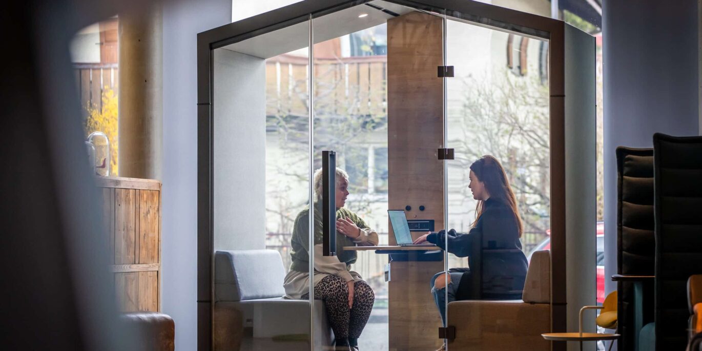 Zwei Personen im modernen Besprechungsraum mit Glaswänden – ein Beispiel dafür, wie professionelle Büroplanung effiziente und zugleich vertrauliche Arbeitsumgebungen schafft.