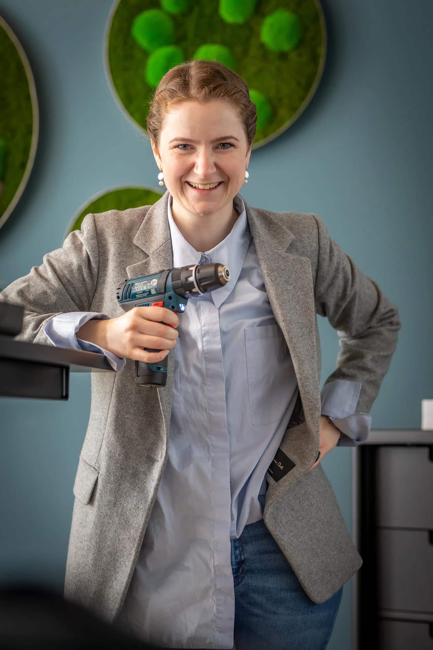 Junge Frau im Business-Outfit hält einen Akkuschrauber in der Hand – bereit für jede Reparaturen.